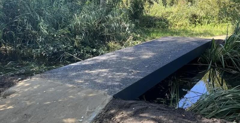 slootje met simpele overbrugging van beton, de sloot is omgeven door groen, riet en gras.