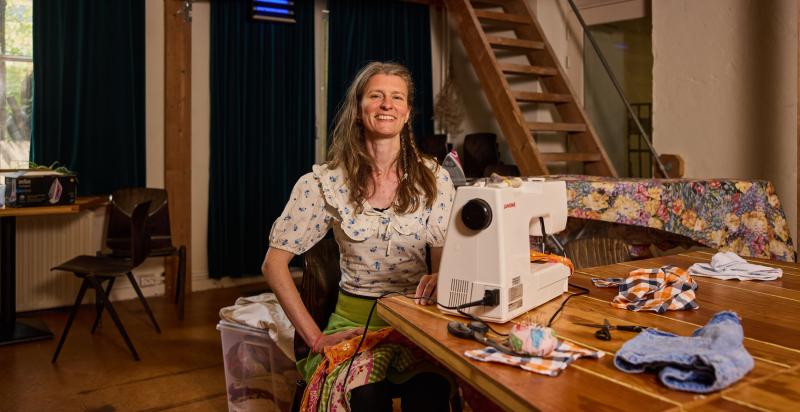 Kunstenaar Emma Hazenzak, poseert in huis aan een houten tafel in huis achter de naaimachine.