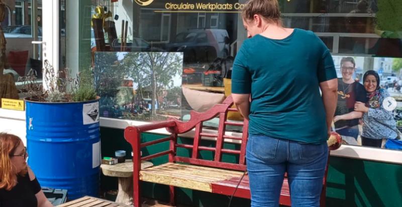 Op de foto twee personen die meubels aan het opknappen zijn op de stoep voor Gouwe Klouwe.