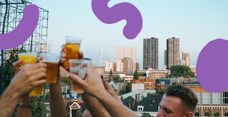 Mensen heffen bekertjes met bier voor de skyline van Rotterdam