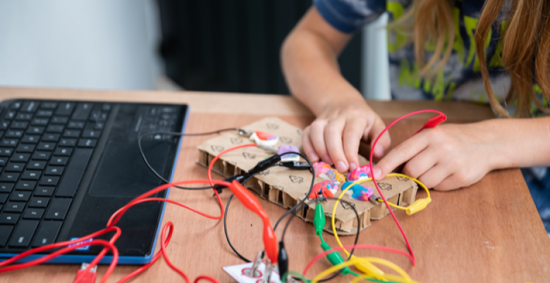 Een kind zit aan tafel en knutselt met allerlei materialen.