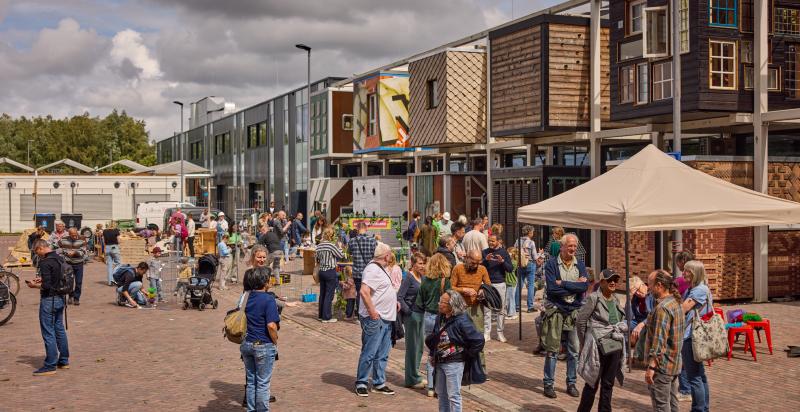 Op de foto mensen die rondlopen over het terrein van Milieupark + De HER. Op de achtergrond circulair centrum De HER.