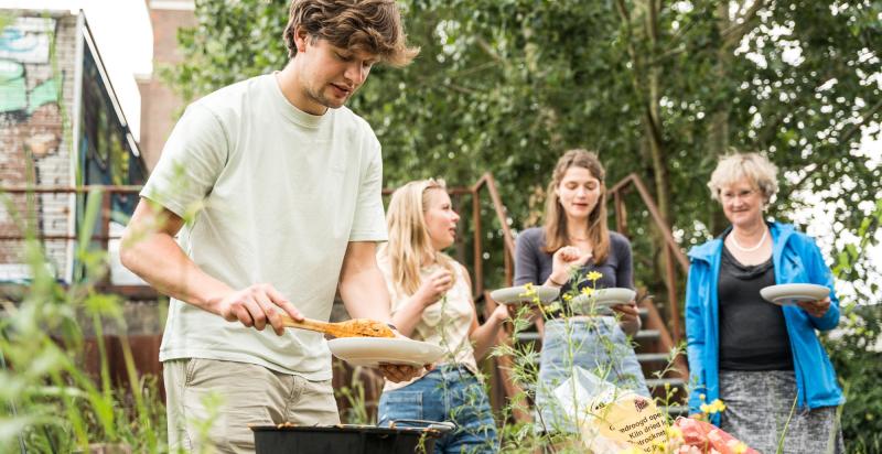 Mensen koken op een barbecue en hebben een bordje vast. Ze zijn in de natuur
