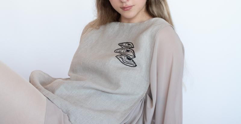 Vrouw zit in een grijze trui met donker borduursel op de stof