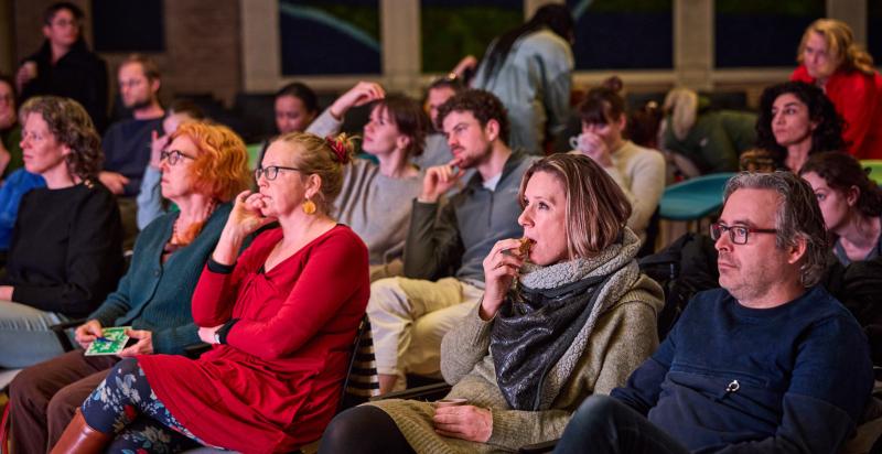 Groep mensen in een zaaltje kijkt samen naar een film.