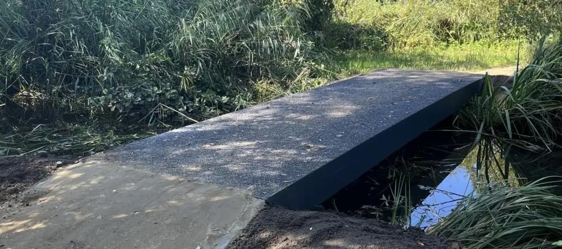 slootje met simpele overbrugging van beton, de sloot is omgeven door groen, riet en gras.