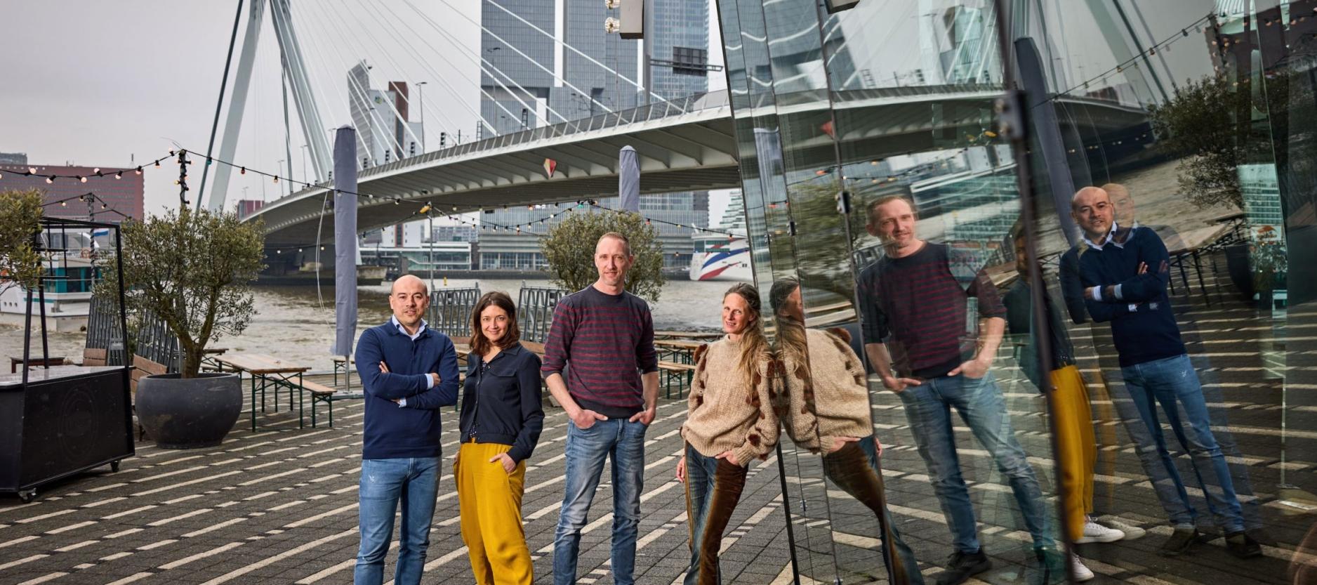 geposeerde foto met Chris de Pagter, Noortje Schrauwen, Kevin de Mutsert en Brontë Flecker op het terras van café Prachtig, met op de achtergrond de Erasmusbrug en het hoge gebouw 'De Rotterdam'.
