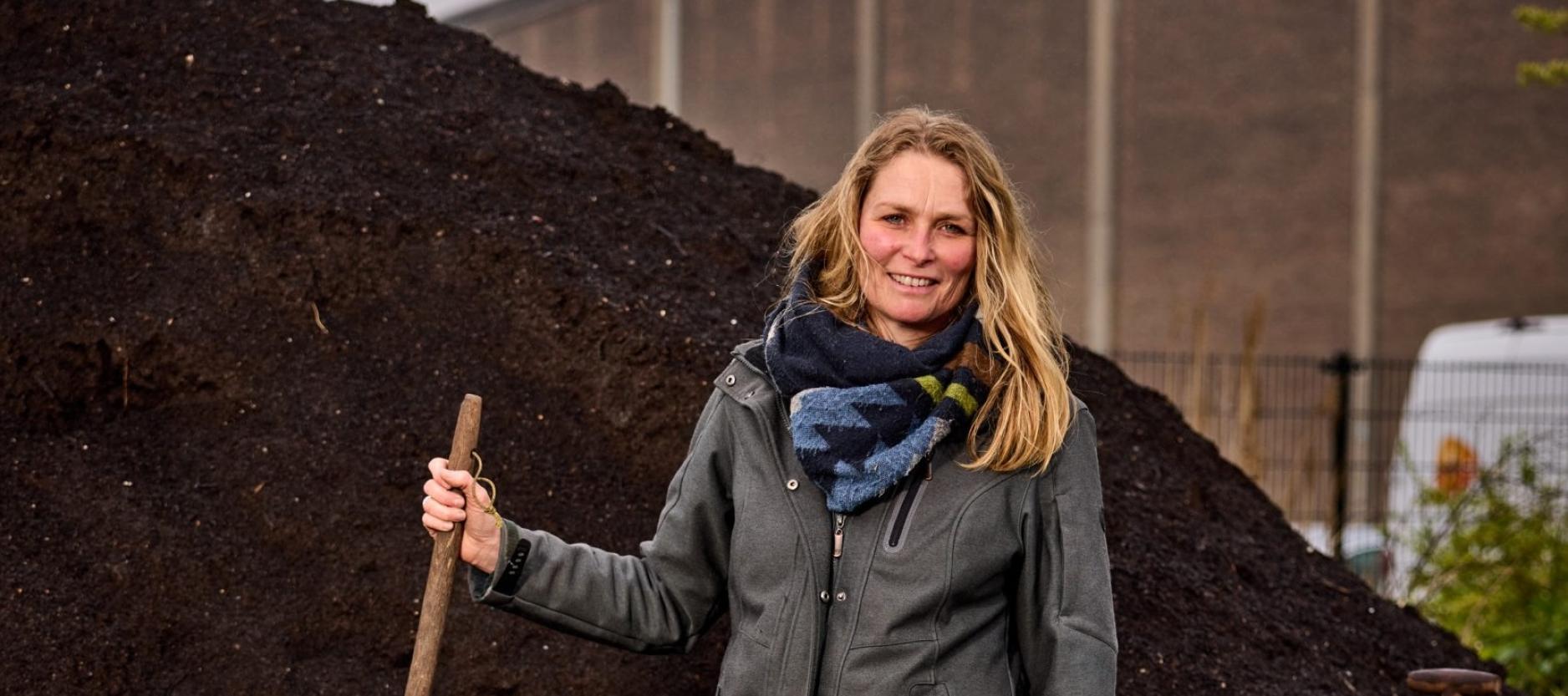 portret foto vrouw met schep in de hand voor een hoge composthoop
