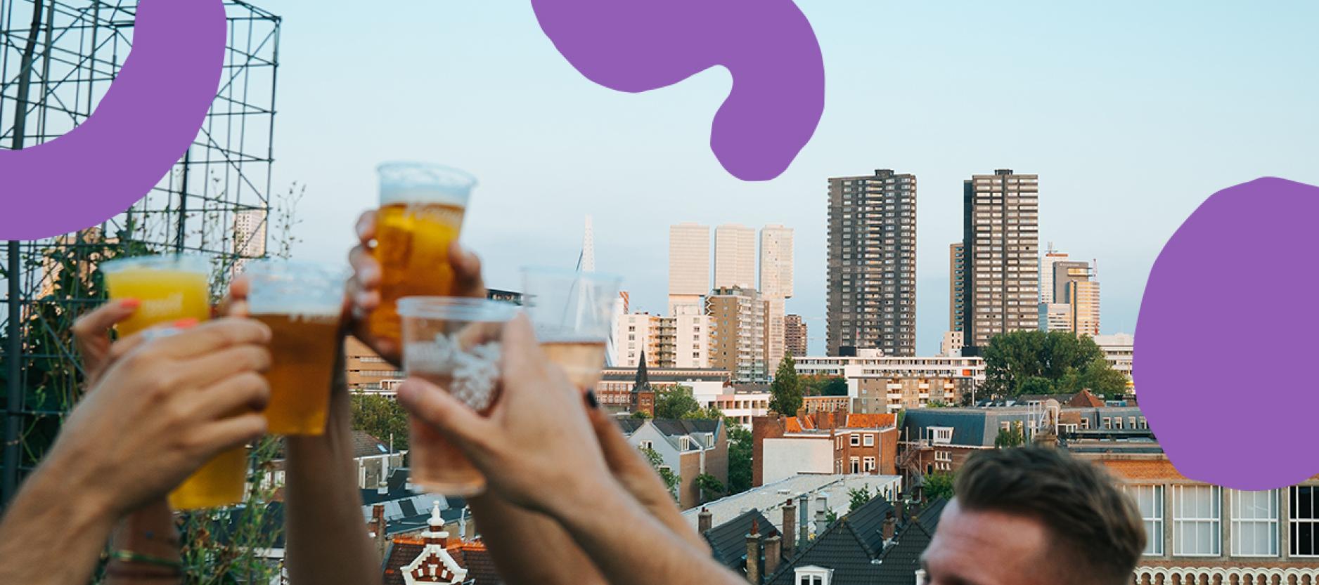 Mensen heffen bekertjes met bier voor de skyline van Rotterdam