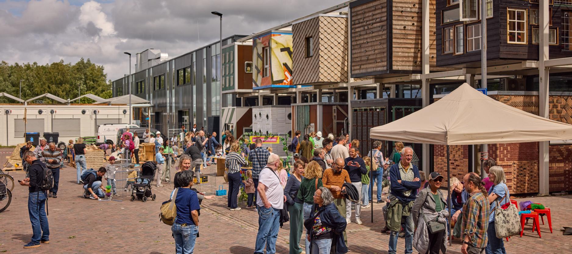 Op de foto mensen die rondlopen over het terrein van Milieupark + De HER. Op de achtergrond circulair centrum De HER.