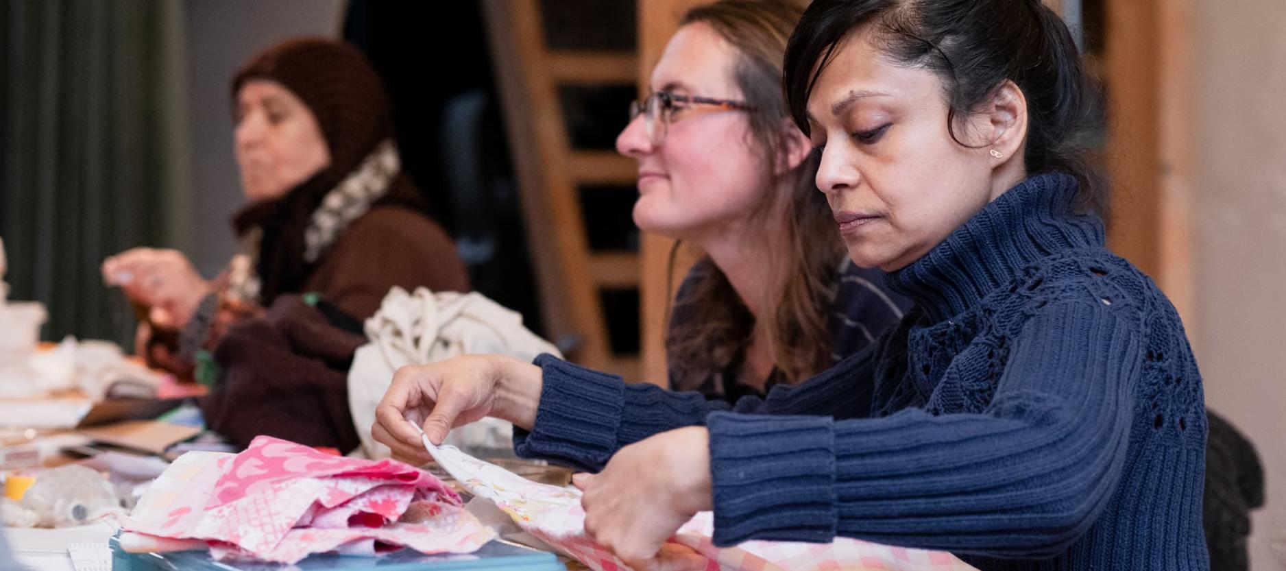 Drie dames zitten aan een tafel kleding te repareren.