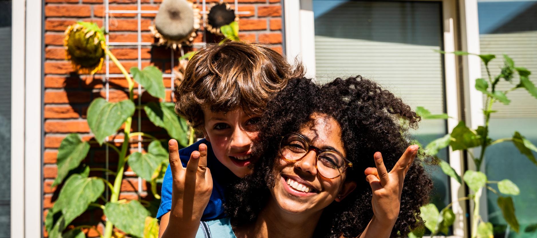 Twee kinderen poseren lachend voor zonnebloemen