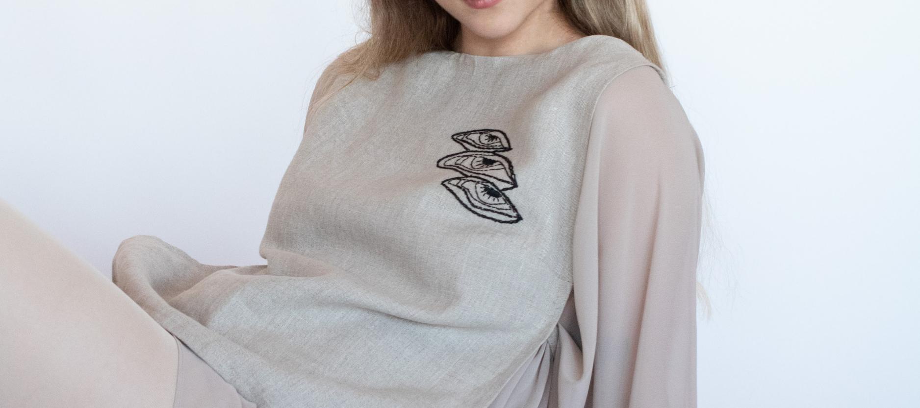 Vrouw zit in een grijze trui met donker borduursel op de stof