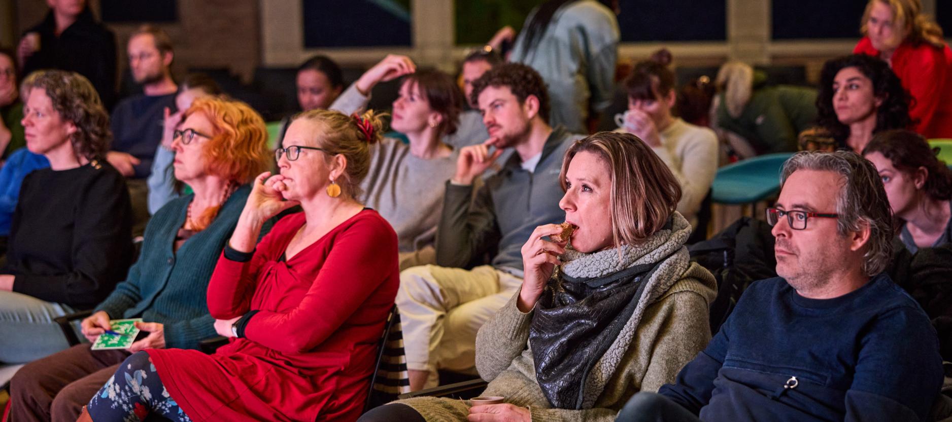 Groep mensen in een zaaltje kijkt samen naar een film.