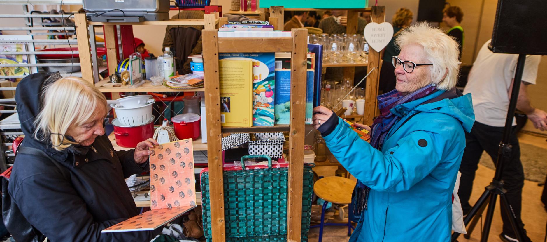 Twee oudere dames bekijken spullen in een weggeefwinkel.