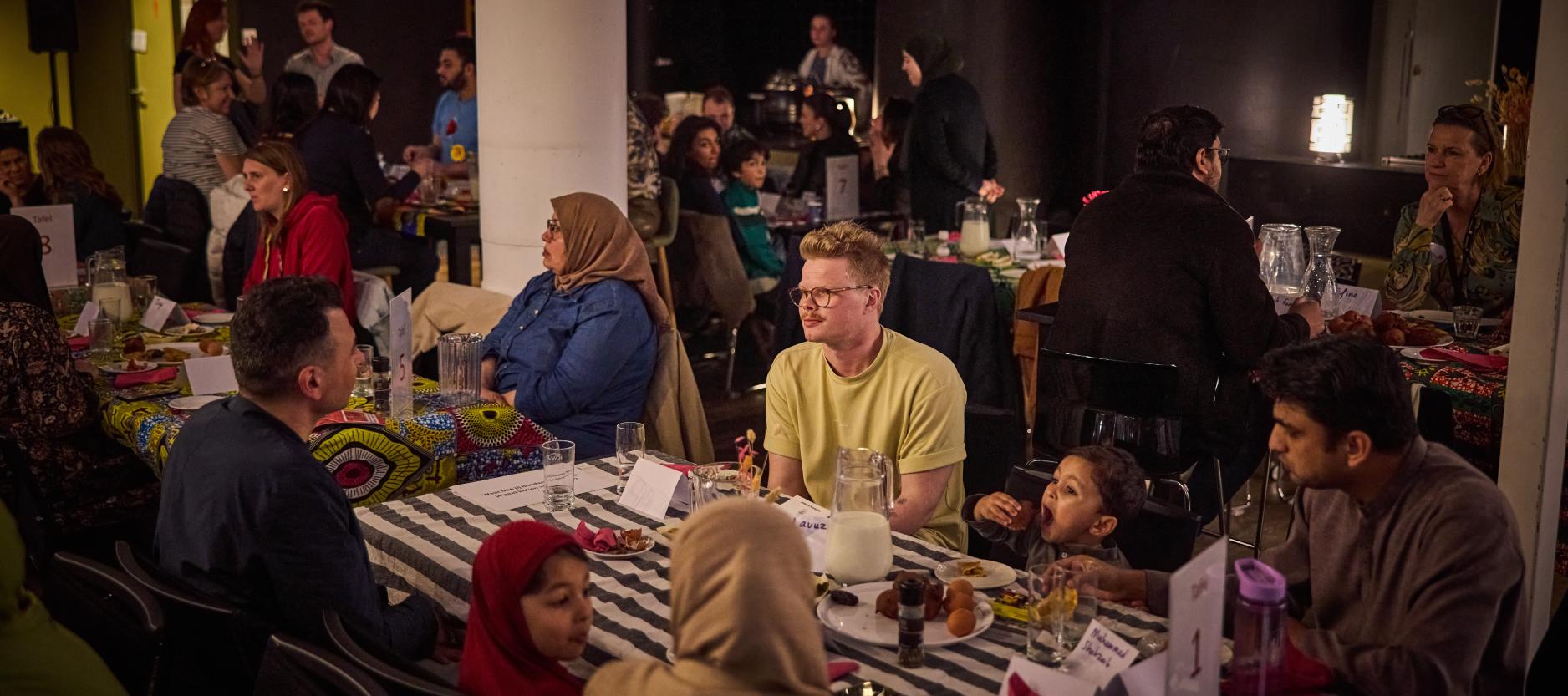 Groep mensen zit samen aan lange tafel te eten.