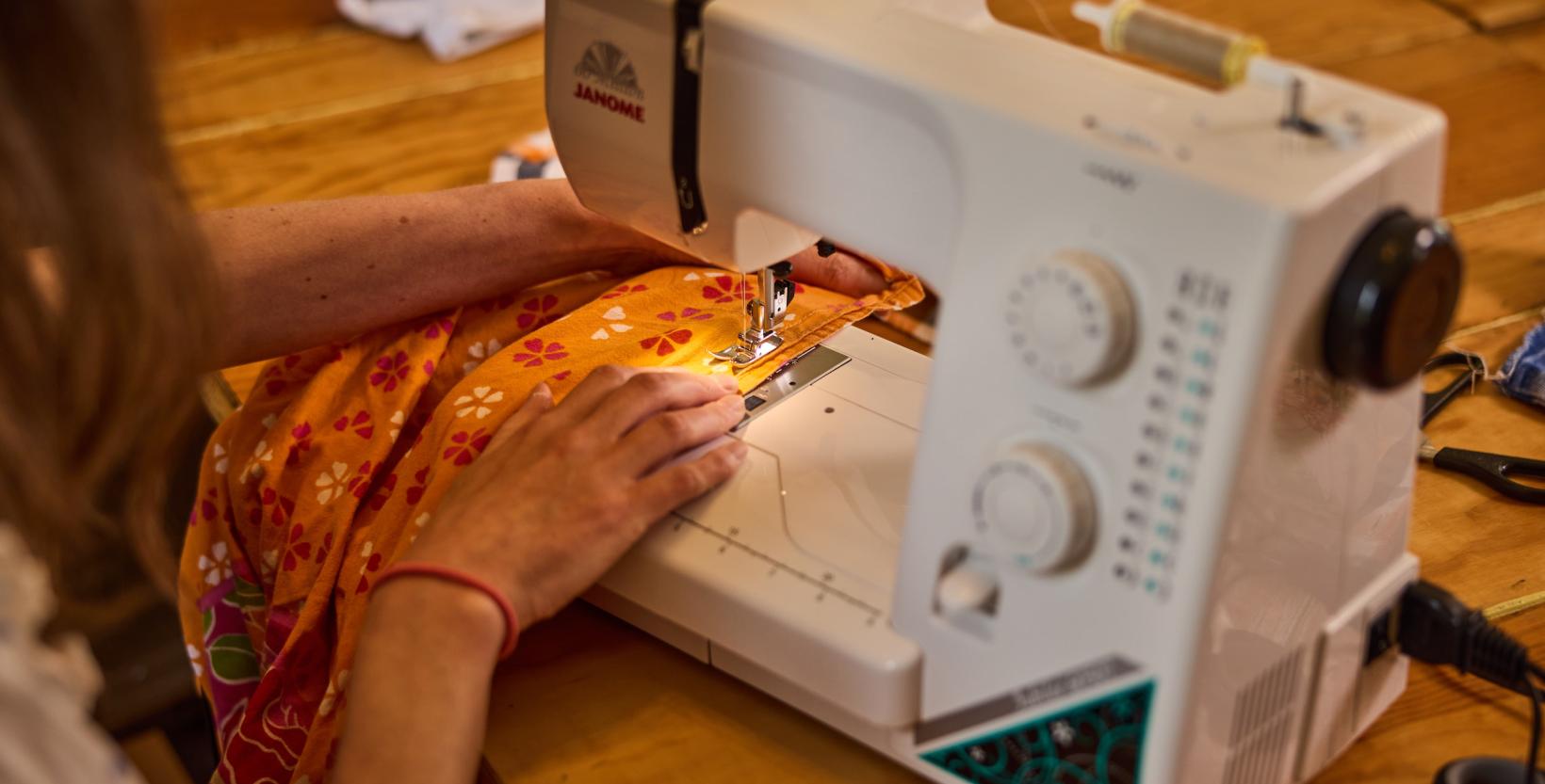 close-up van handen Emma Hazenak haalt stof door de naaimachine