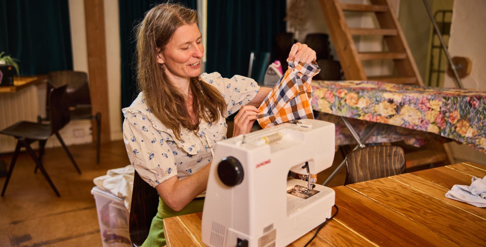 Emma Hazenak aan een houten tafel aan het werk achter de naaimachine.