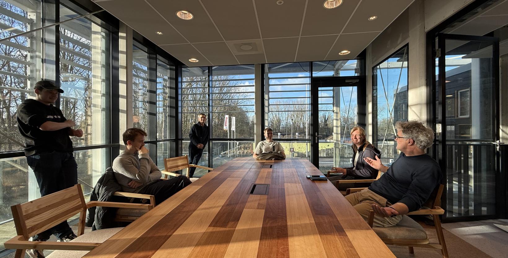 Groep mensen zit om een houten tafel in de vergaderzaal van circulair centrum De HER.