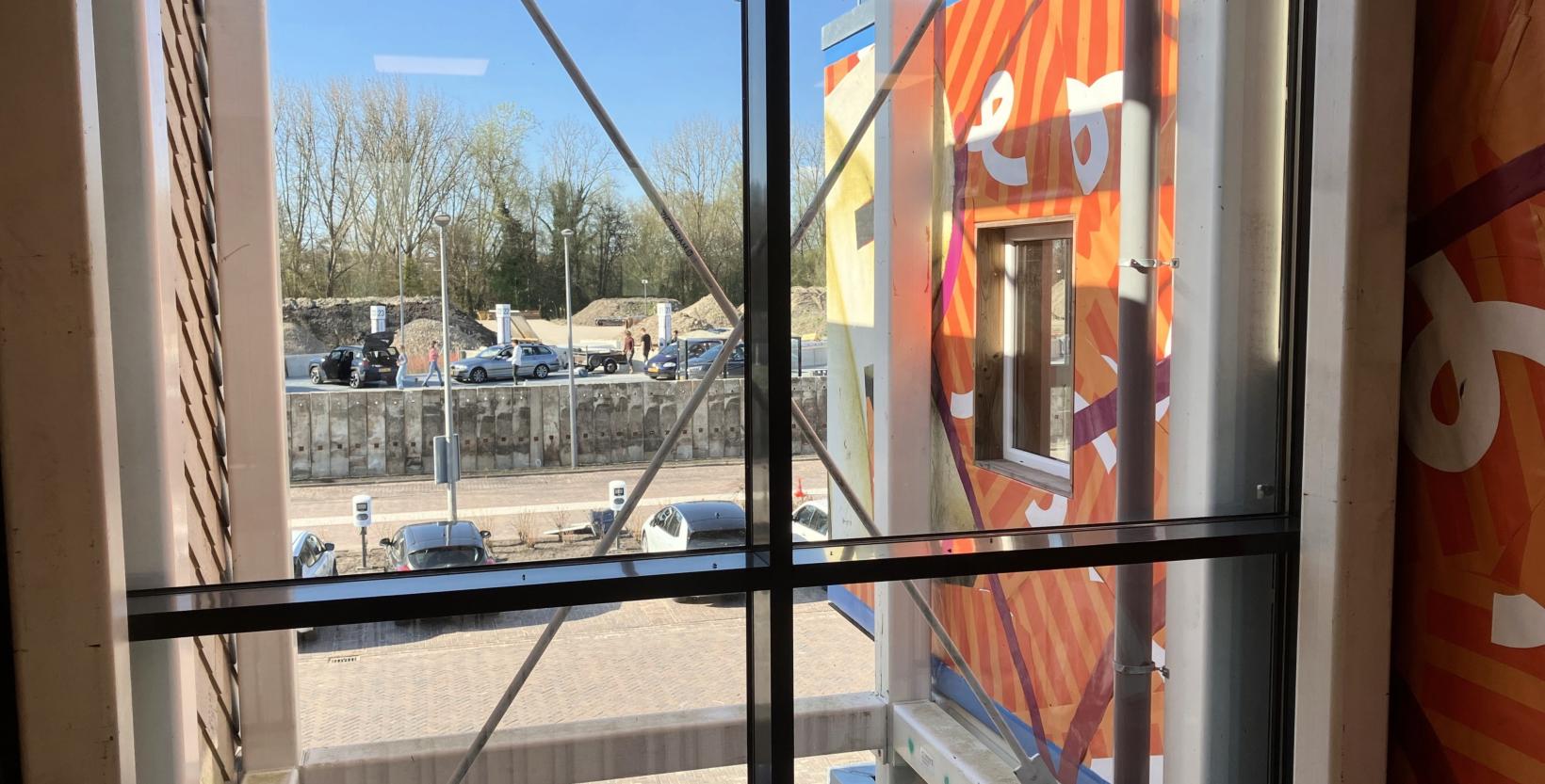 Doorkijkje door het raam van de eerste verdieping van circulair centrum De HER met uitzicht op het milieupark.