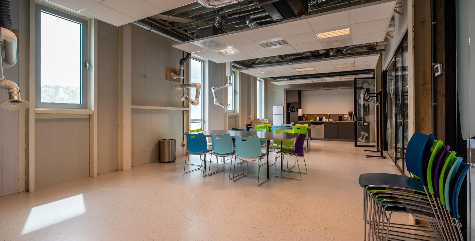 Educatieve ruimte in circulair Centrum De HER. Een grote, lichte ruimte met een keukenblok en tafels en stoelen. 