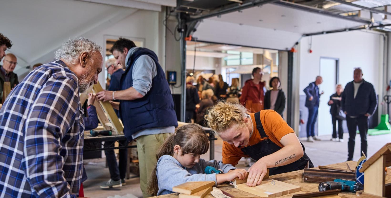 Vrouw helpt een klein meisje met het timmeren van een houten constructie.