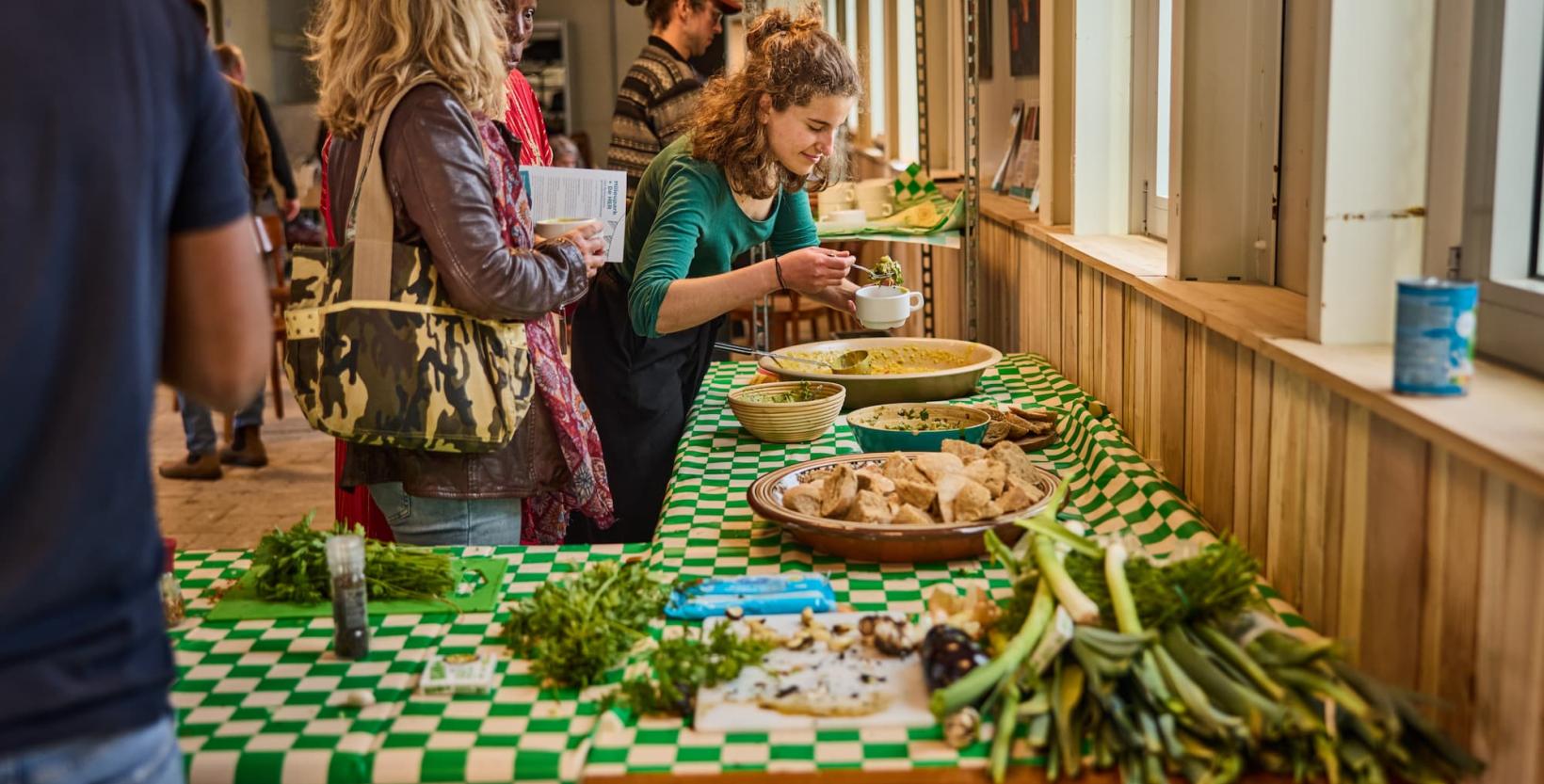 Een vrouw loopt langs een tafel met eten en schept iets op.