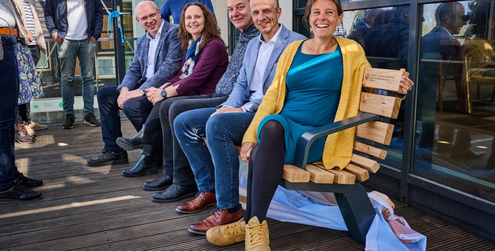 Vijf mensen zitten op een bankje gemaakt van circulair stadshout