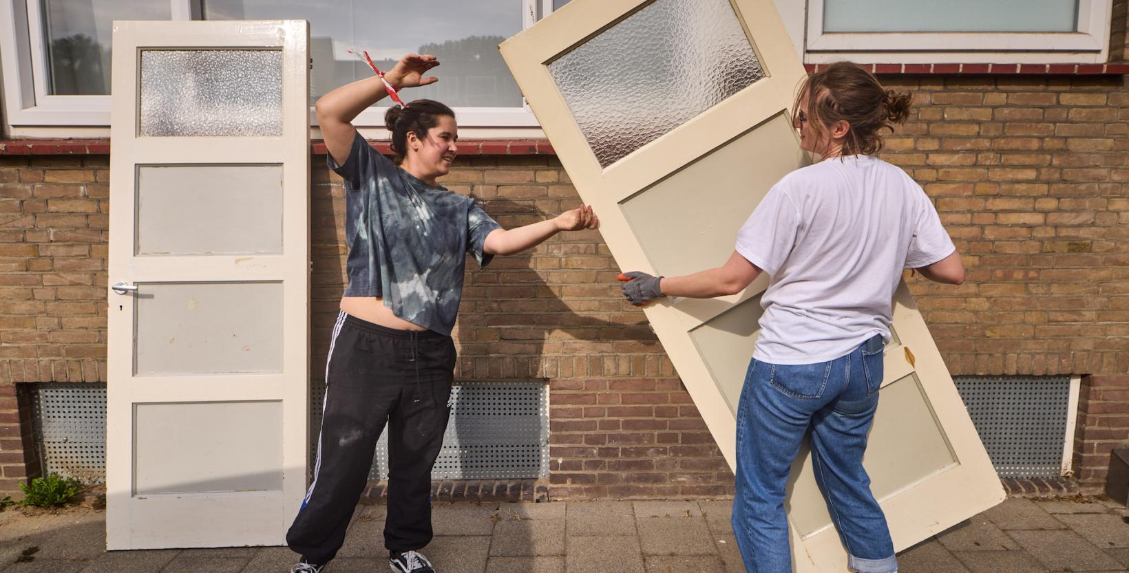 Twee mensen tillen samen een houten deur op de stoep.
