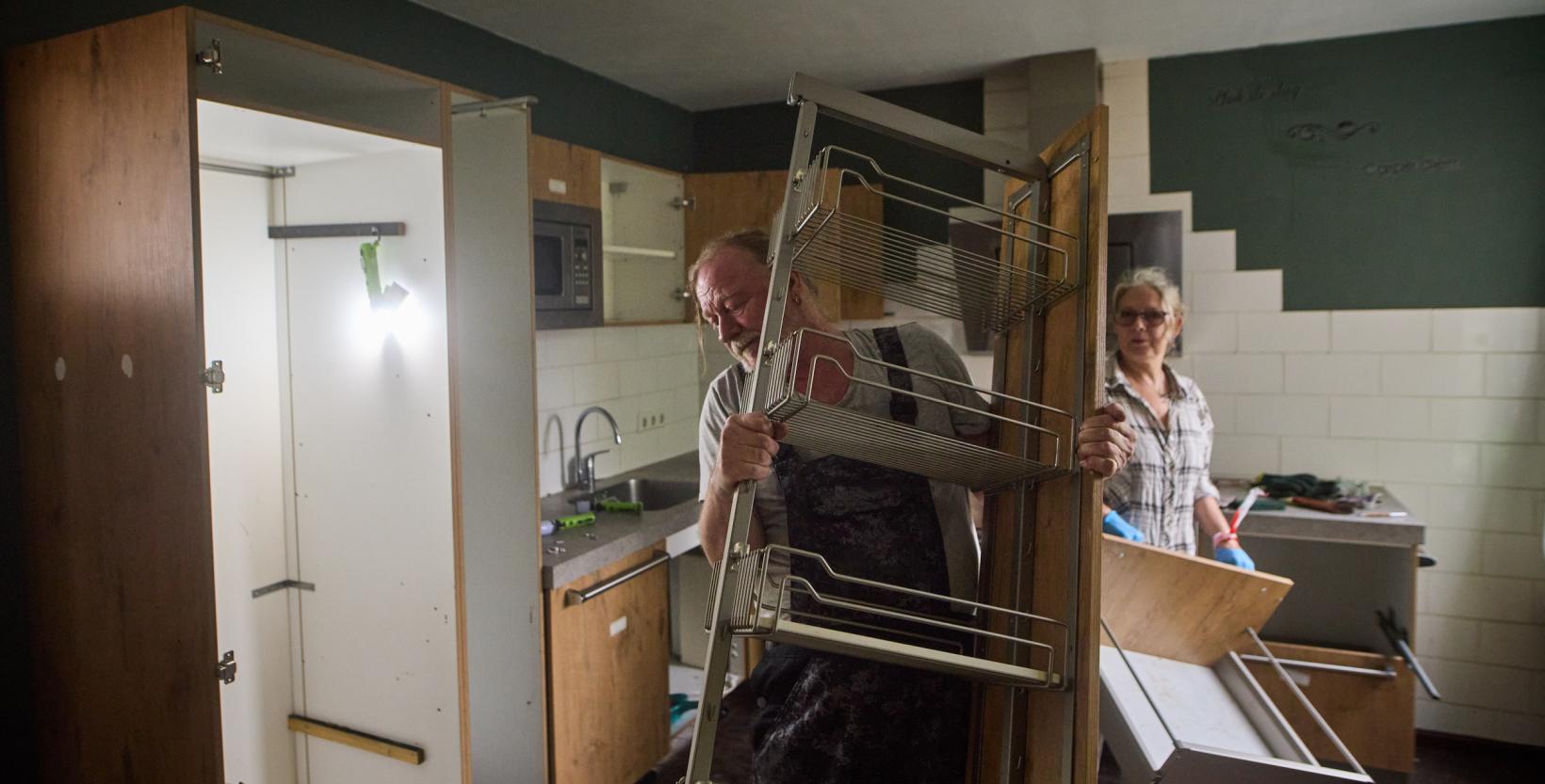 Man en vrouw halen een keuken uit elkaar; de man draagt een kastdeel met rekken, de vrouw houdt een lade vast.