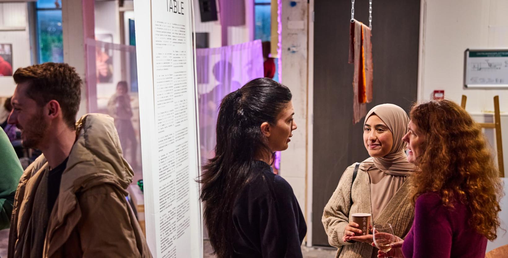 Aantal mensen in gesprek bij de opening van de tentoonstelling AYNI in circulair centrum De HER.